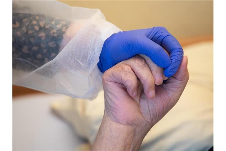 Eine Altenpflegerin in Schutzkleidung hält die Hand eines Bewohners. Foto: Sebastian Gollnow/dpa/Symbolbild
