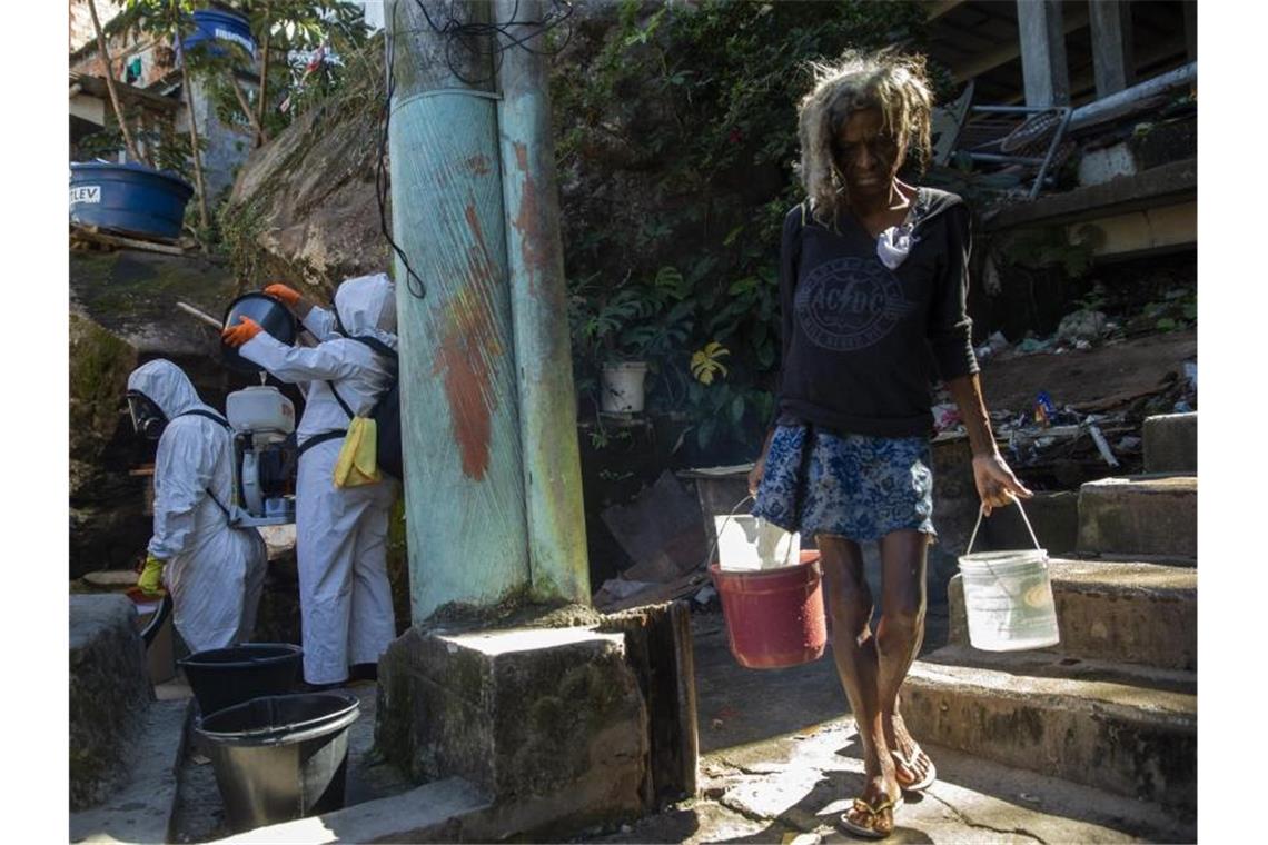 Eine Bewohnerin in einer Favela in Rio de Janeiro holt Wasser, während Freiwillige versuchen das Viertel zu desinfizieren. Foto: Fernando Souza/dpa
