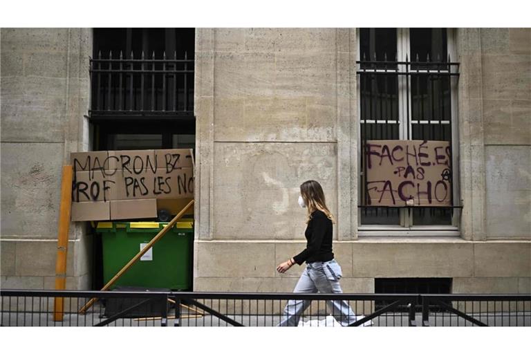 Eine Demonstrantin geht an Plakaten vorbei, auf denen steht „Macron, fick deine Lehrerin, nicht unsere“ (l) und „Wütend, keine Faschisten“ (r), während der Blockade eines Gebäudes der Sciences Politiques im Rahmen der landesweiten Proteste.