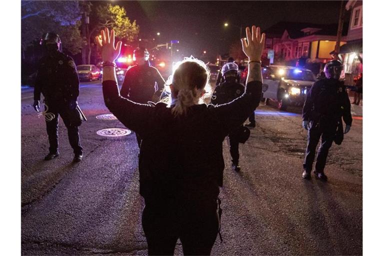 Eine Demonstrantin steht bei einem Protest gegen Polizeigewalt in Oakland mit hochgestreckten Armen vor Polizisten. Foto: Ethan Swope/AP/dpa