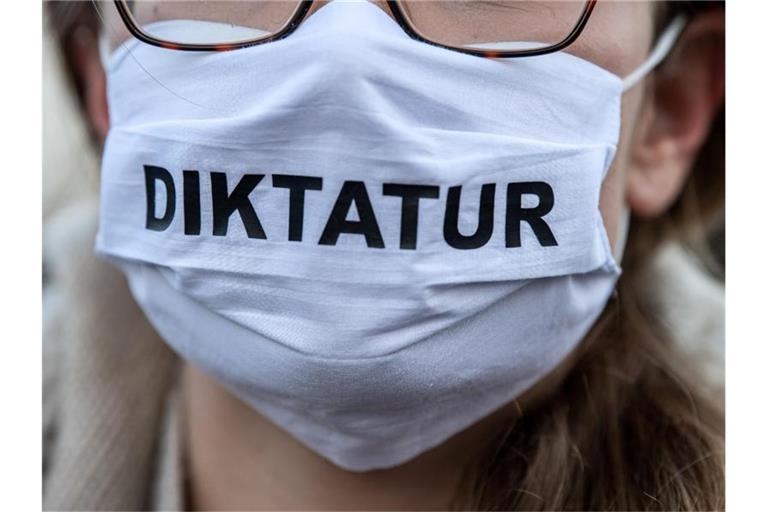 Eine Demonstrantin trägt eine Maske mit der Aufschrift „Diktatur“. Foto: Sina Schuldt/dpa/archivbild
