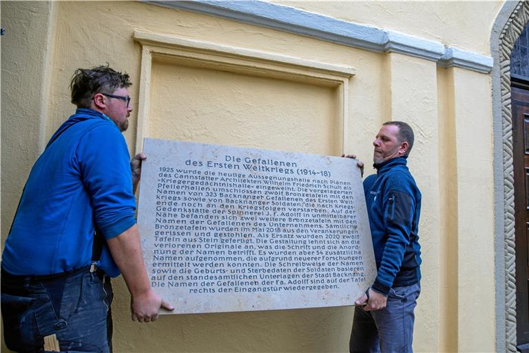 Eine der Steintafeln ist bereits fertiggestellt. Auf ihr wird die Historie des Gedenkens erinnert, inklusive des schändlichen Diebstahls. Carl-Eugen Vogt (rechts) und sein Geselle Markus Lutz präsentieren die Platte vor ihrem künftigen Platz an der Aussegnungshalle. Die restlichen 13 Platten werden den Winter über hergestellt. Die zwölf Haupttafeln mit den Namen aller Backnanger Gefallenen sind jeweils 1,70 Meter hoch. Foto: A. Becher