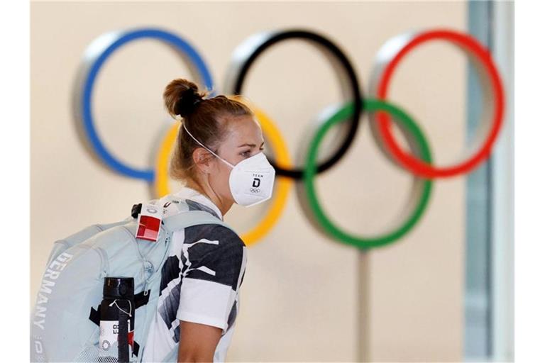 Eine deutsche Athletin trägt eine Schutzmaske und geht bei ihrer Ankunft am Flughafen Haneda an den Olympischen Ringen vorbei. Foto: Uncredited/Kyodo News/AP/dpa