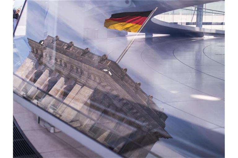 Eine Deutschland-Fahne spiegelt sich in der Kuppel des Reichstagsgebäudes. Foto: Sophia Kembowski/dpa
