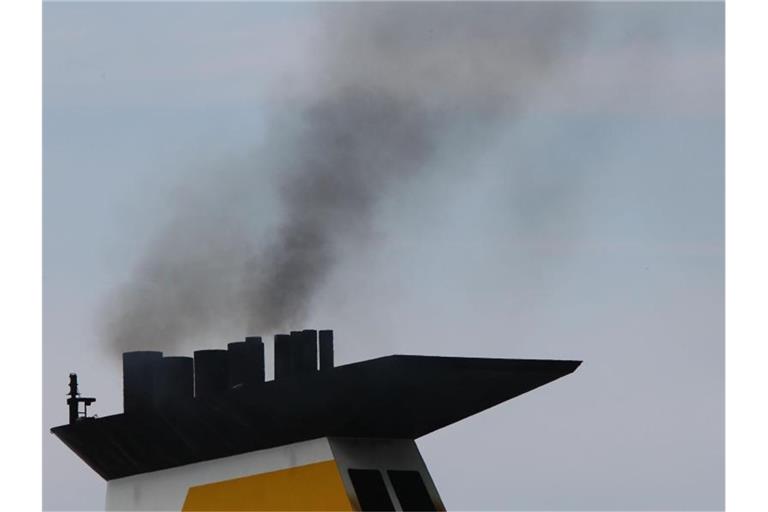 Eine dunkle Abgaswolke steigt aus dem Schornstein eines Fährschiffs bei der Ausfahrt aus dem Seehafen. Foto: Jens Büttner/dpa-Zentralbild/dpa