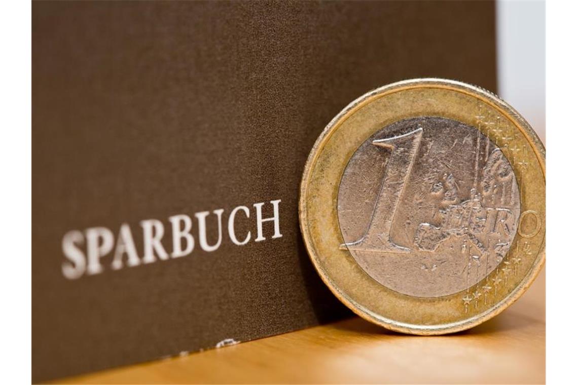 Eine Ein-Euro-Münze steht am neben einem Sparbuch. Foto: Daniel Karmann/Archivbild