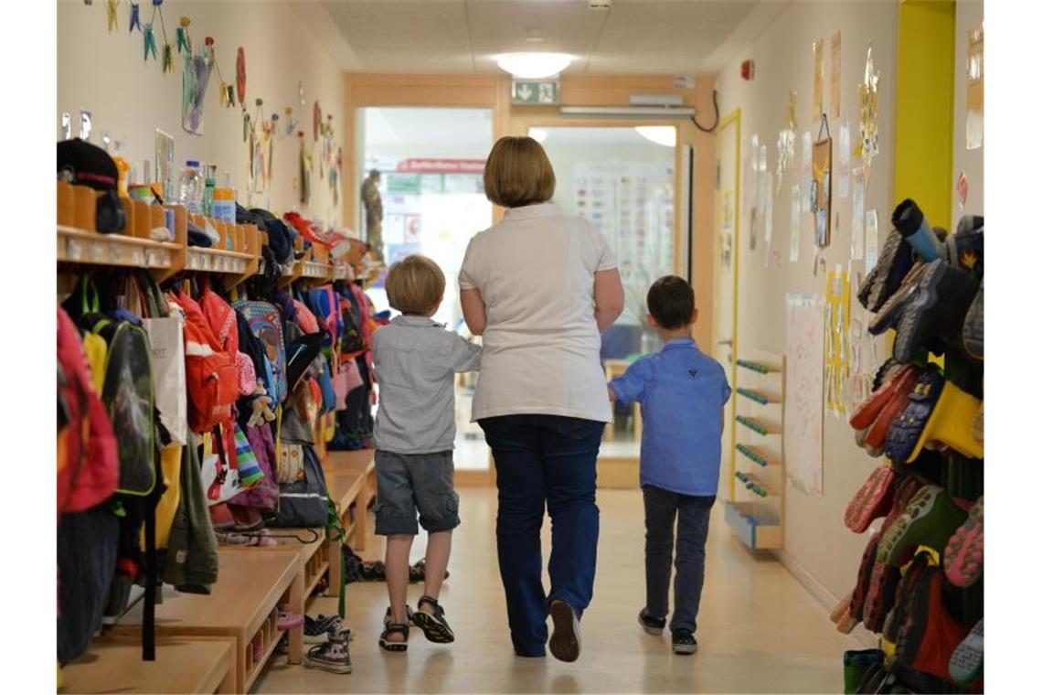 Staatliche Stellen suchen dringend Personal Eine Erzieherin geht in einem Kindergarten mit zwei Kindern über den Flur. Foto: Jan-Philipp Strobel/Archivbild