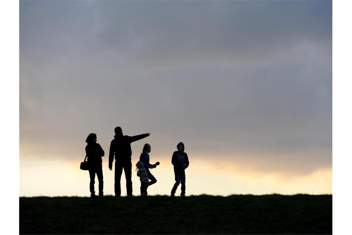Eine Familie beim Spaziergang unterm abendlichen Wolkenhimmel. Foto: picture alliance / dpa