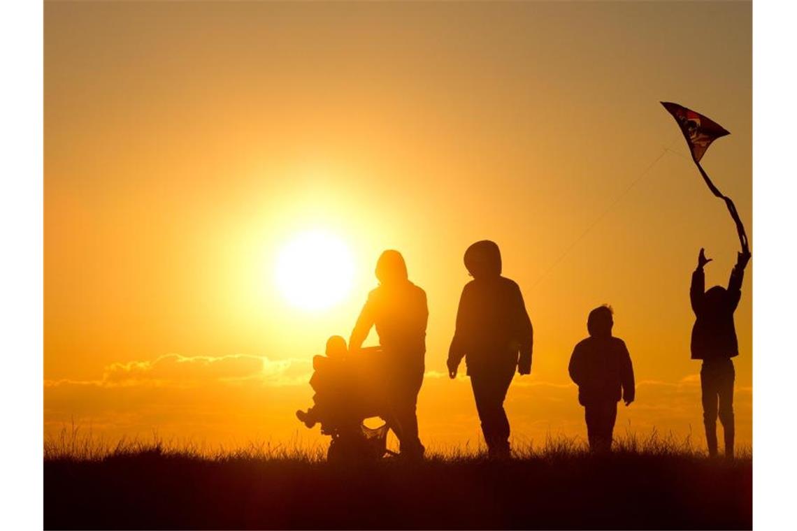 Studie: Warum es sich gut lebt im Süden Eine Familie mit Kinderwagen und einem Drachen geht bei Sonnenuntergang über einen Weg. Foto: Christian Charisius/Archivbild