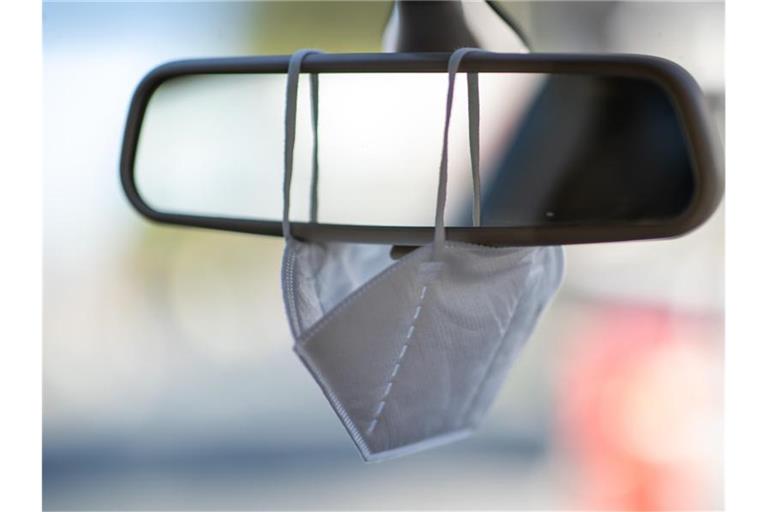 Eine FFP2-Maske hängt am Rückspiegel eines Autos (Symbolbild). Foto: Daniel Karmann/dpa