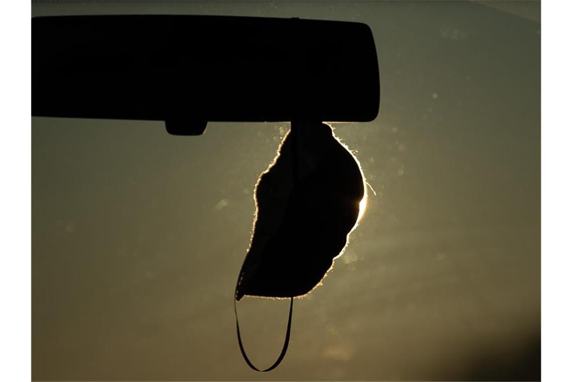 Eine FFP2-Maske hängt vor der aufgehenden Sonne in einem Auto. Foto: Sebastian Gollnow/dpa/Symbolbild