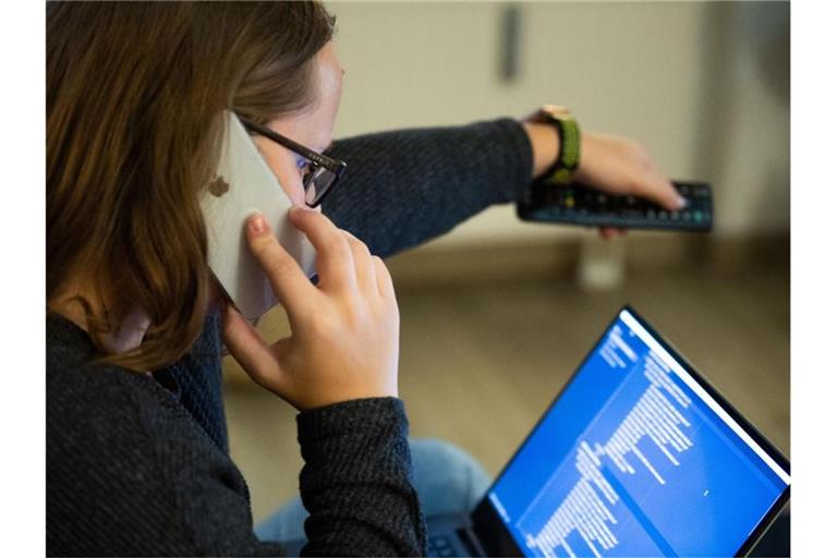 Eine Frau bedient beim Telefonieren einen Fernseher, vor ihr steht ein aufgeklappter Laptop. Neuen Hinweisen zufolge sind Frauen nicht generell besser beim Multitasking als Männer. Foto: Lino Mirgeler/Symbolbild