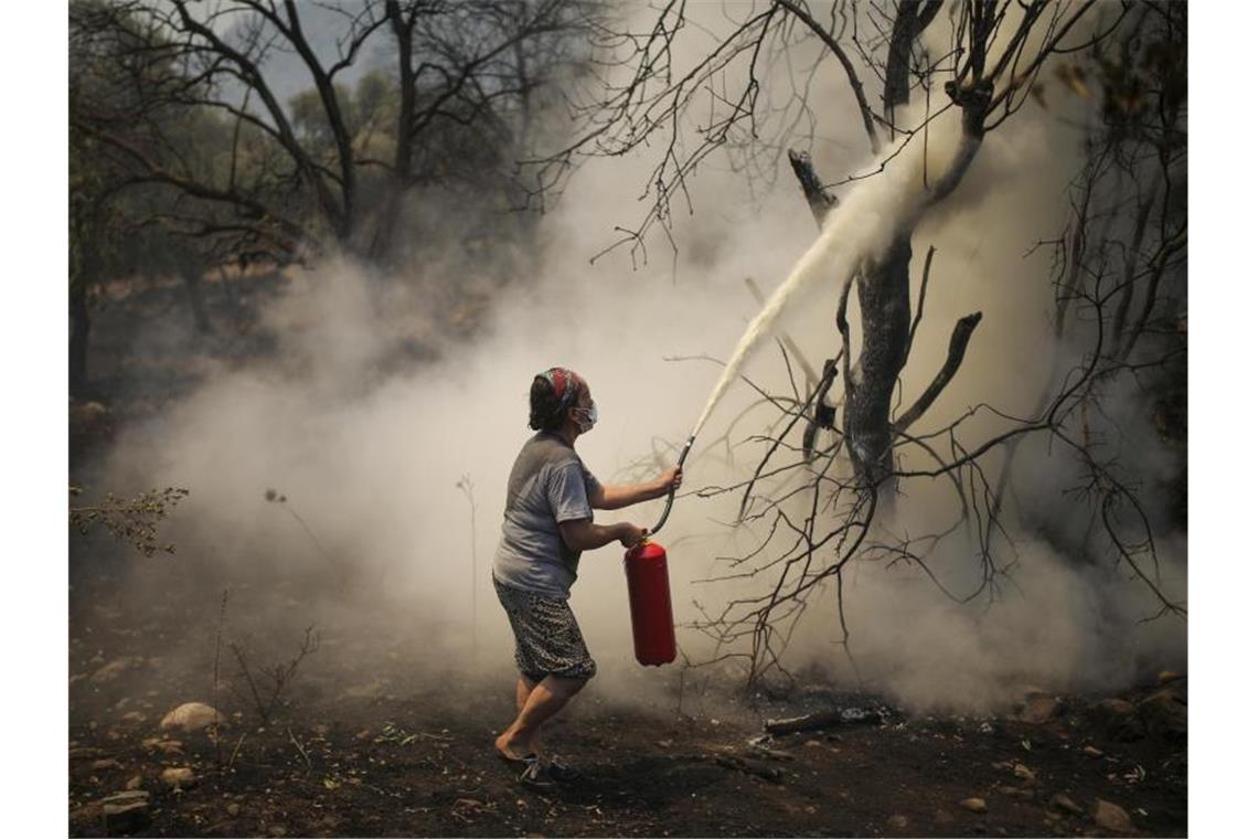 Eine Frau bekämpft mit einem Feuerlöscher einen Waldbrand im Dorf Cokertme. Foto: Emre Tazegul/AP/dpa
