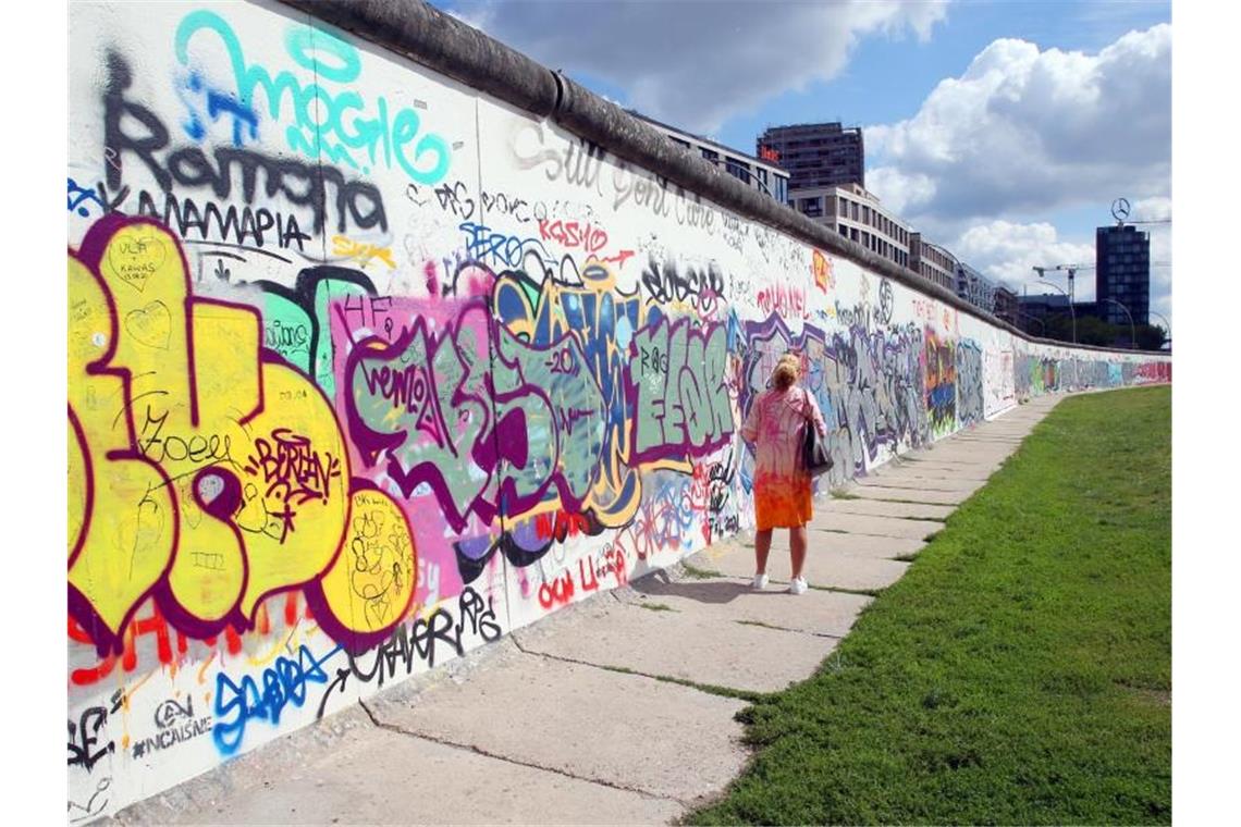 Eine Frau betrachtet an der East Side Galery im Bezirk Friedrichshain-Kreuzberg die bemalten Betonsegmente der Berliner Mauer. Foto: Wolfgang Kumm/dpa