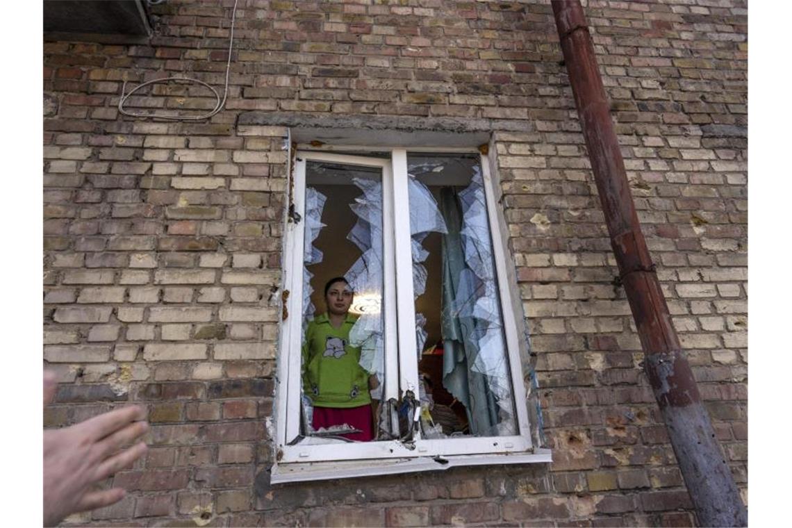 Eine Frau blickt durch ein zerstörtes Fenster ihrer durch Beschuss beschädigten Wohnung in Kiew. Foto: Rodrigo Abd/AP/dpa