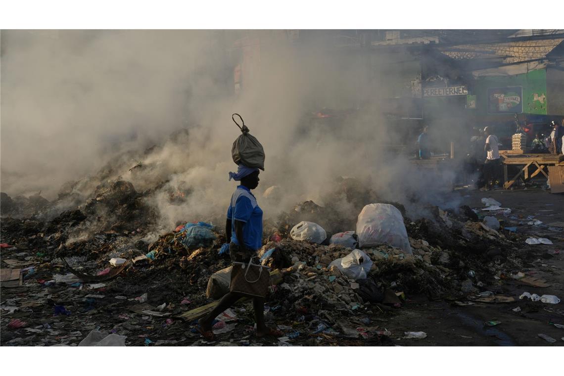 Eine Frau, die eine Tasche auf dem Kopf trägt, geht im Stadtteil Petion-Ville von Port-au-Prince an schwelendem Müll vorbei.