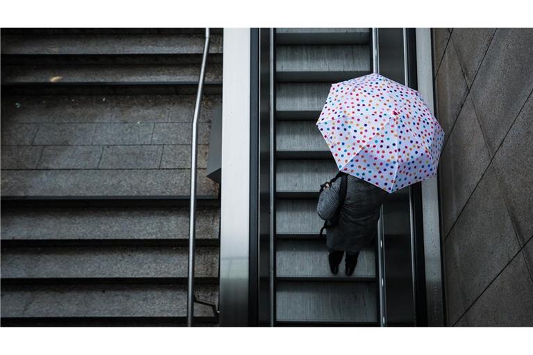 Eine Frau fährt mit ihrem Regenschirm eine Rolltreppe hinauf. Das Wetter soll in der Region Stuttgart in den nächsten Tagen wechselhaft bleiben.