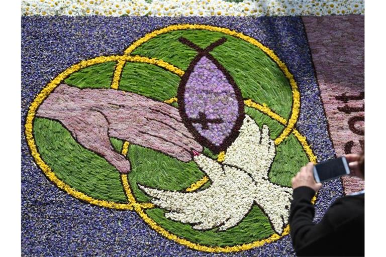 Eine Frau fotografiert an Fronleichnam während der Prozession Kirchenmotive in einem Blumenteppich. Foto: Patrick Seeger/Archivbild
