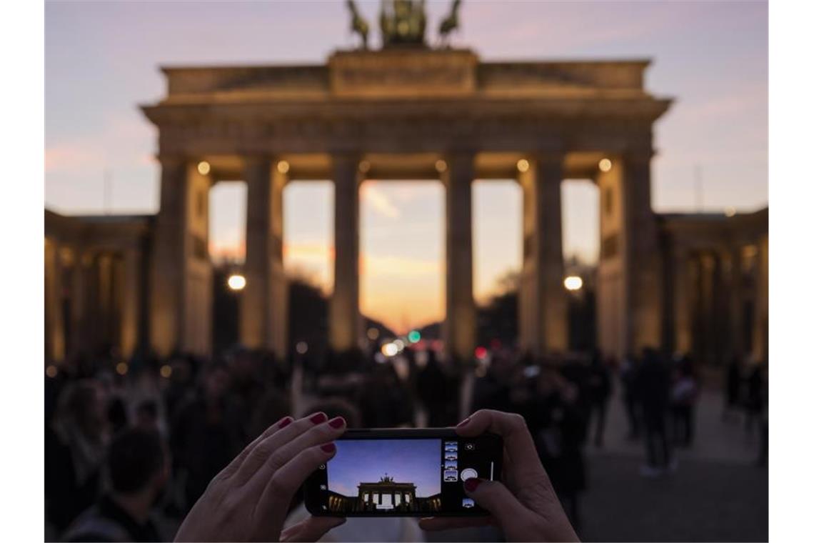 Ranking: Darmstadt ist Zukunft, Berlin ist Dynamik Eine Frau fotografiert das Brandenburger Tor in der Abenddämmerung. Foto: Christoph Soeder/dpa