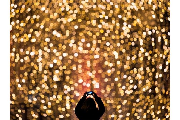 Eine Frau fotografiert die Fassade eines mit Lichterketten weihnachtlich geschmückten Einkaufszentrums. Foto: Daniel Reinhardt/dpa