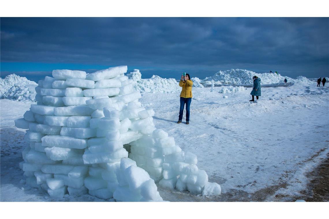 Eine Frau fotografiert ein aus Eisstücken gebautes Iglu vor meterhohen Eisbergen am Ostseestrand auf der Insel Usedom.