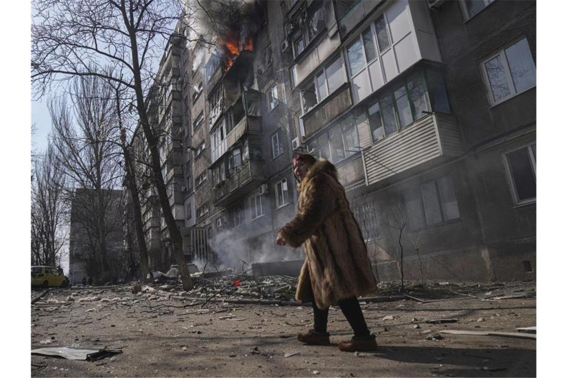 Wohl mehr Personen in Theater in Mariupol als angenommen Eine Frau geht an einem brennenden Wohnhaus vorbei, nachdem es beschossen wurde. Foto: Evgeniy Maloletka/AP/dpa