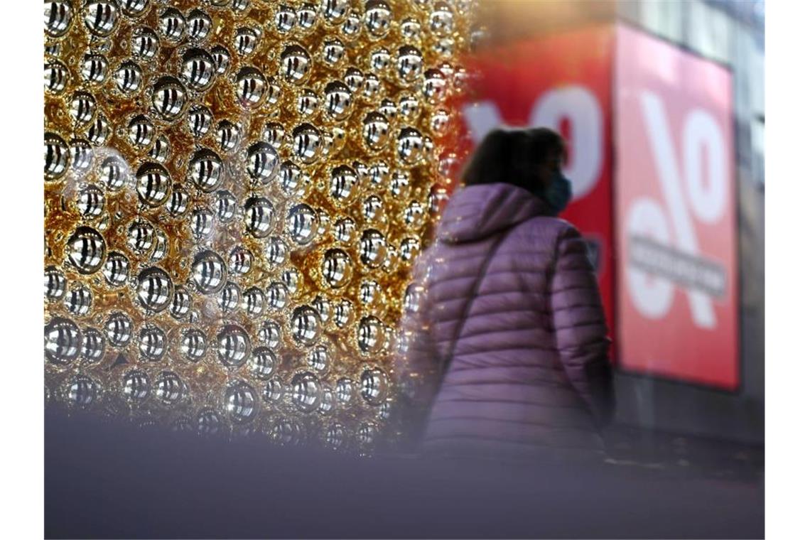Eine Frau geht an einem mit Weihnachtskugeln geschmücktem Schaufenster vorbei. Foto: Marijan Murat/dpa