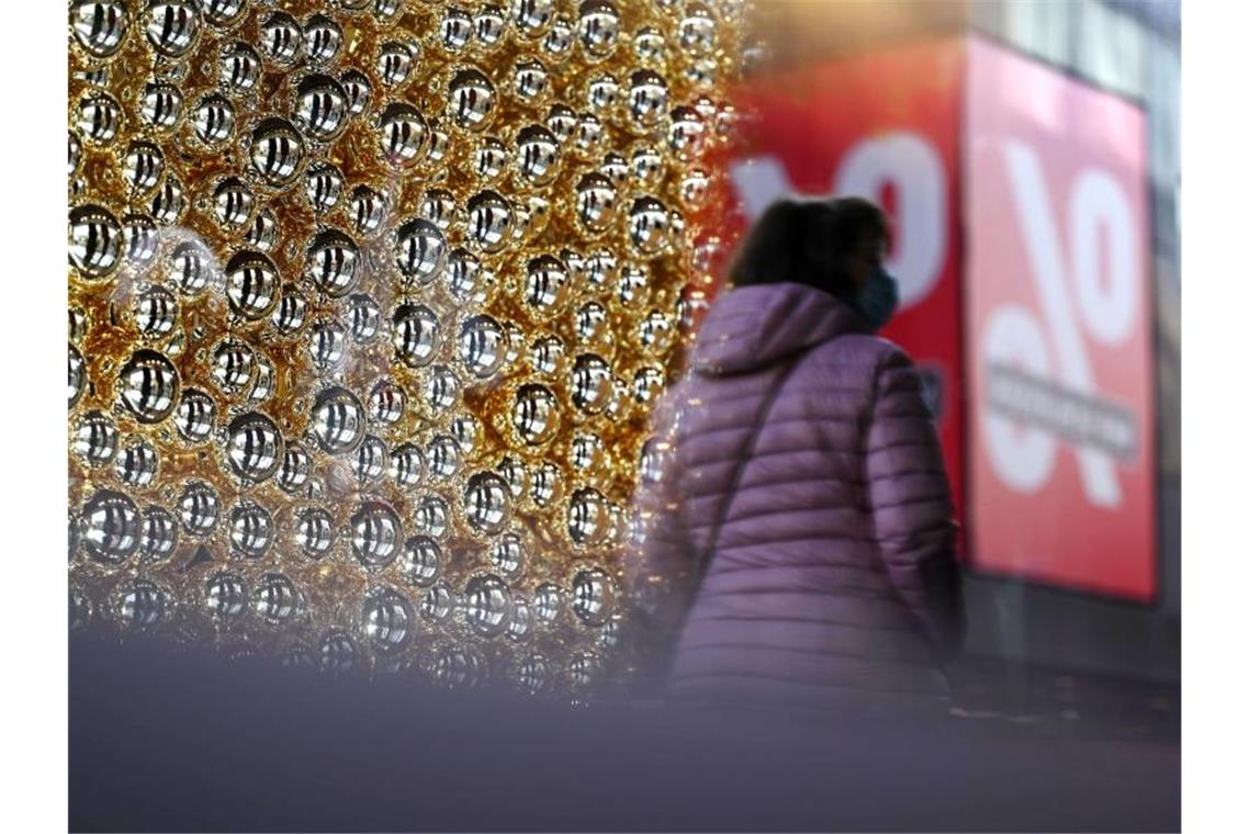Eine Frau geht an einem mit Weihnachtskugeln geschmücktem Schaufenster vorbei. Foto: Marijan Murat/dpa