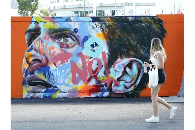 Eine Frau geht an einem Wandbild von Novak Djokovic vorbei, das auf eine Wand im Melbourne Park gemalt wurde. Foto: Dave Hunt/AAP/dpa
