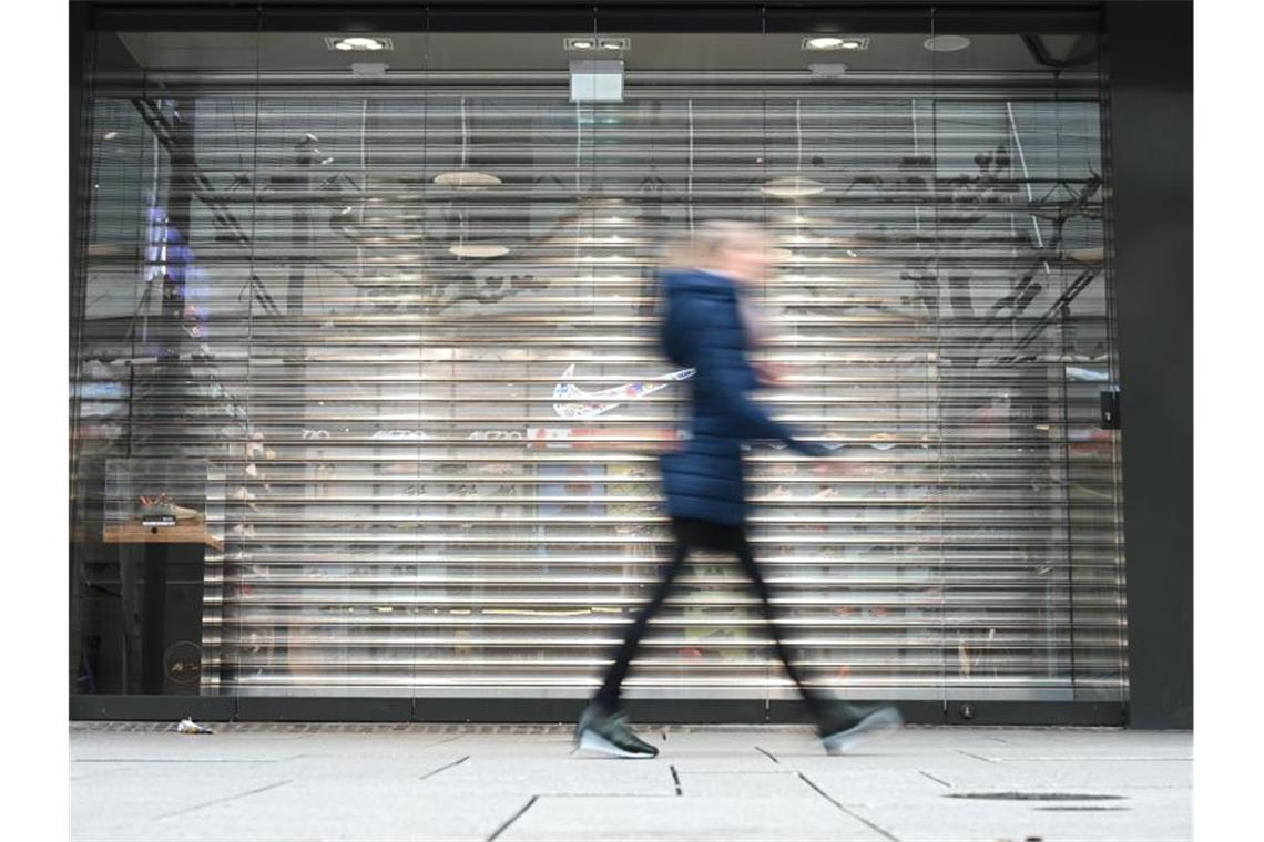 Eine Frau geht auf der Frankfurter Einkaufsmeile Zeil an einem Geschäft vorbei, an dem noch das Rollgitter heruntergelassen ist. Durch die Corona-Krise droht vielen innerstädtischen Geschäften das Aus. Foto: Arne Dedert/dpa