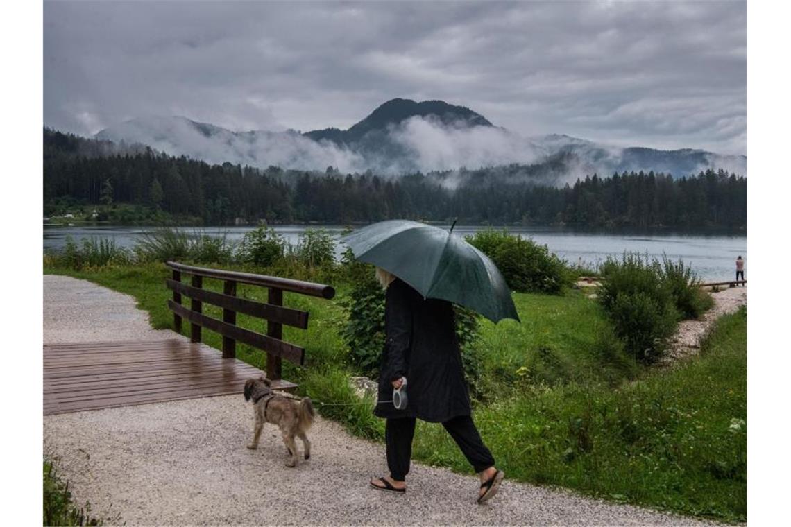 Eine Frau geht bei Regen mit ihrem Hund am Hintersee in Ramsau Bei Berchtesgaden spazieren. Foto: Lino Mirgeler