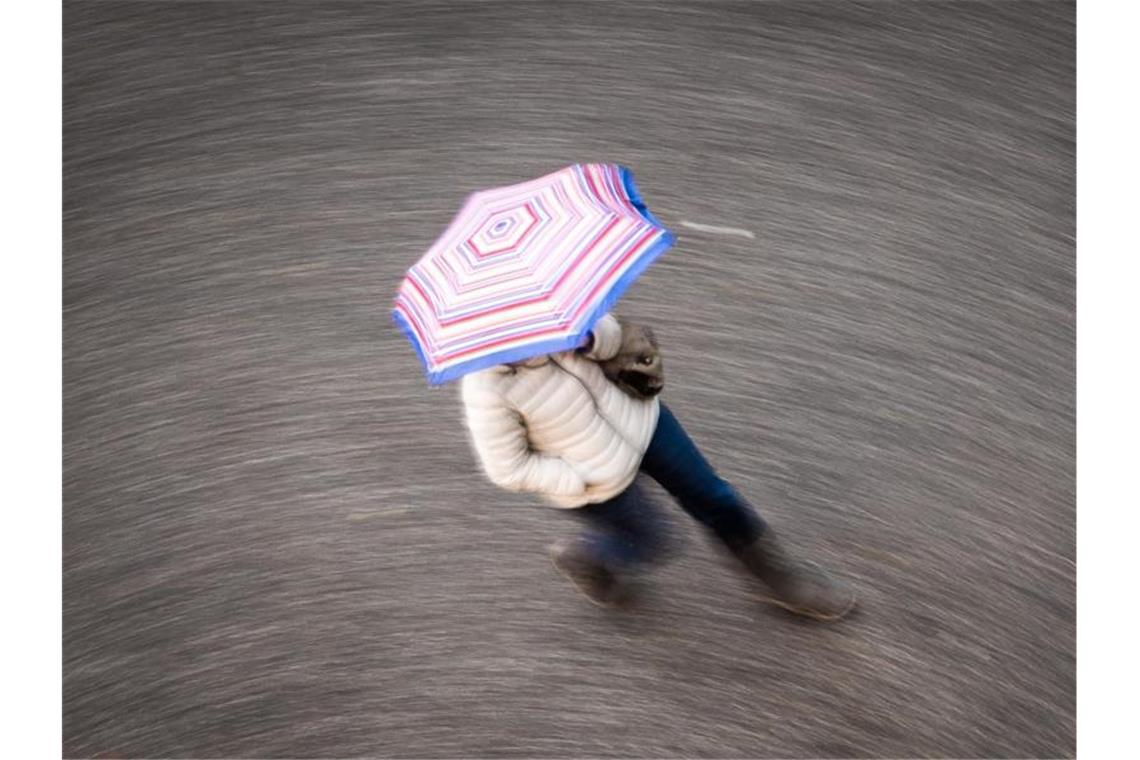 Nass-grauer Start ins Wochenende Eine Frau geht bei regnerischem Wetter über eine Straße. Foto: Frank Rumpenhorst/dpa/Symbolbild