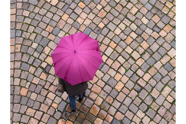 Eine Frau geht mit einem Regenschirm auf einer Straße entlang. Foto: Sebastian Kahnert/dpa-Zentralbild/dpa/Symbolbild