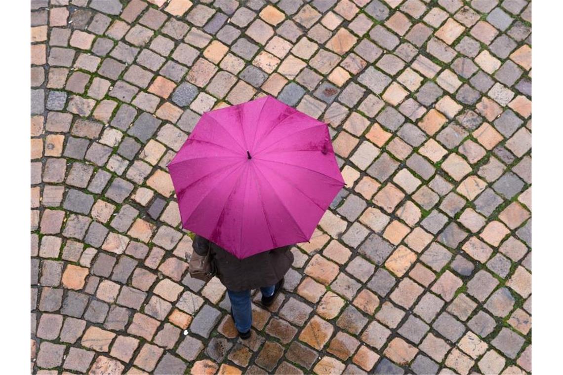 Eine Frau geht mit einem Regenschirm auf einer Straße entlang. Foto: Sebastian Kahnert/dpa-Zentralbild/dpa/Symbolbild