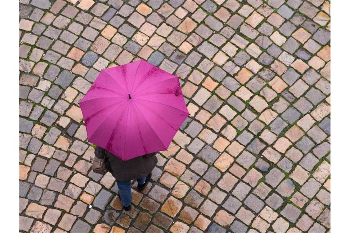 Eine Frau geht mit einem Regenschirm auf einer Straße mit Kopfsteinpflaster entlang. Foto: Sebastian Kahnert/dpa-Zentralbild/dpa/Archivbild