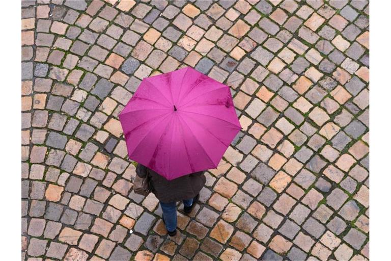 Eine Frau geht mit einem Regenschirm auf einer Straße mit Kopfsteinpflaster entlang. Foto: Sebastian Kahnert/dpa-Zentralbild/dpa/Archivbild