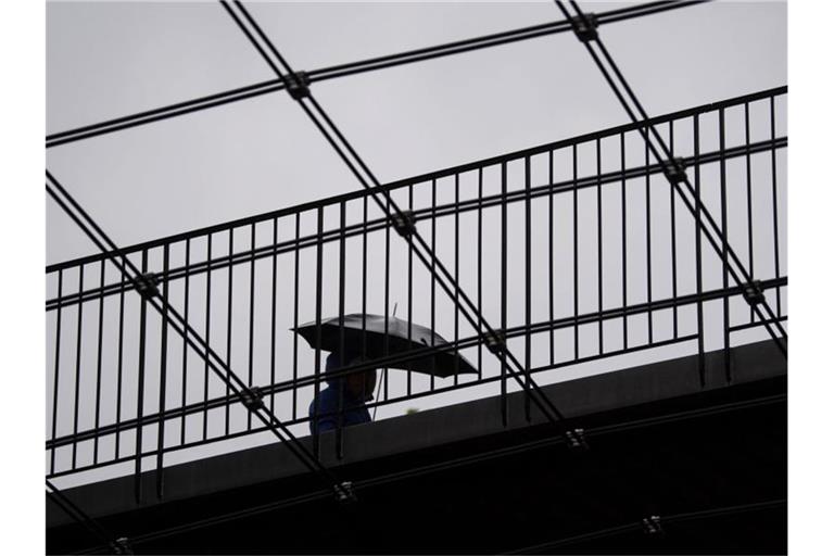 Eine Frau geht mit ihrem Regenschirm über eine Brücke. Foto: Marijan Murat/dpa/Symbolbild