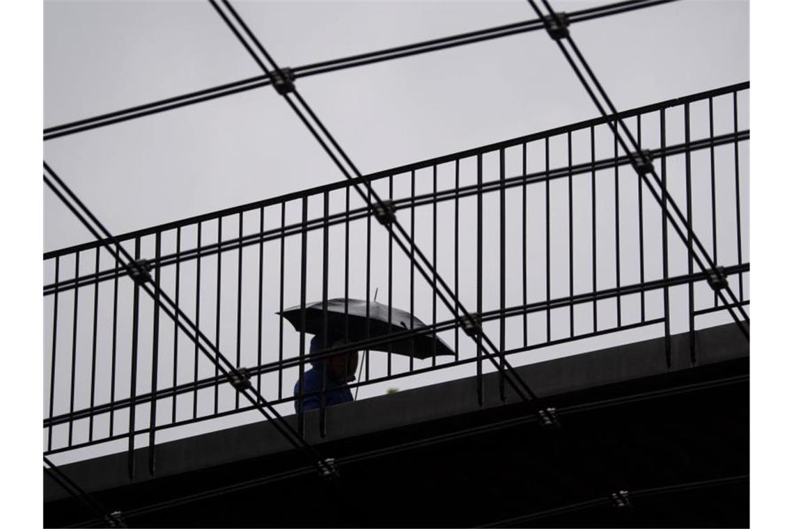 Eine Frau geht mit ihrem Regenschirm über eine Brücke. Foto: Marijan Murat/dpa/Archivbild