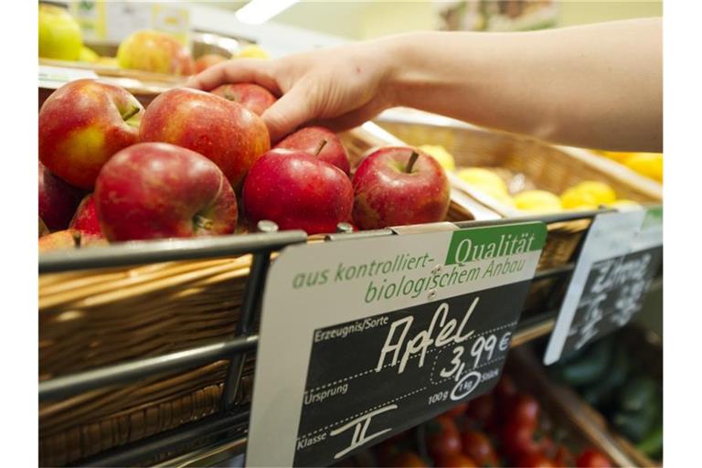 Eine Frau greift nach einem Apfel aus dem Obst- und Gemüseregal eines Reformhauses. Foto: Inga Kjer