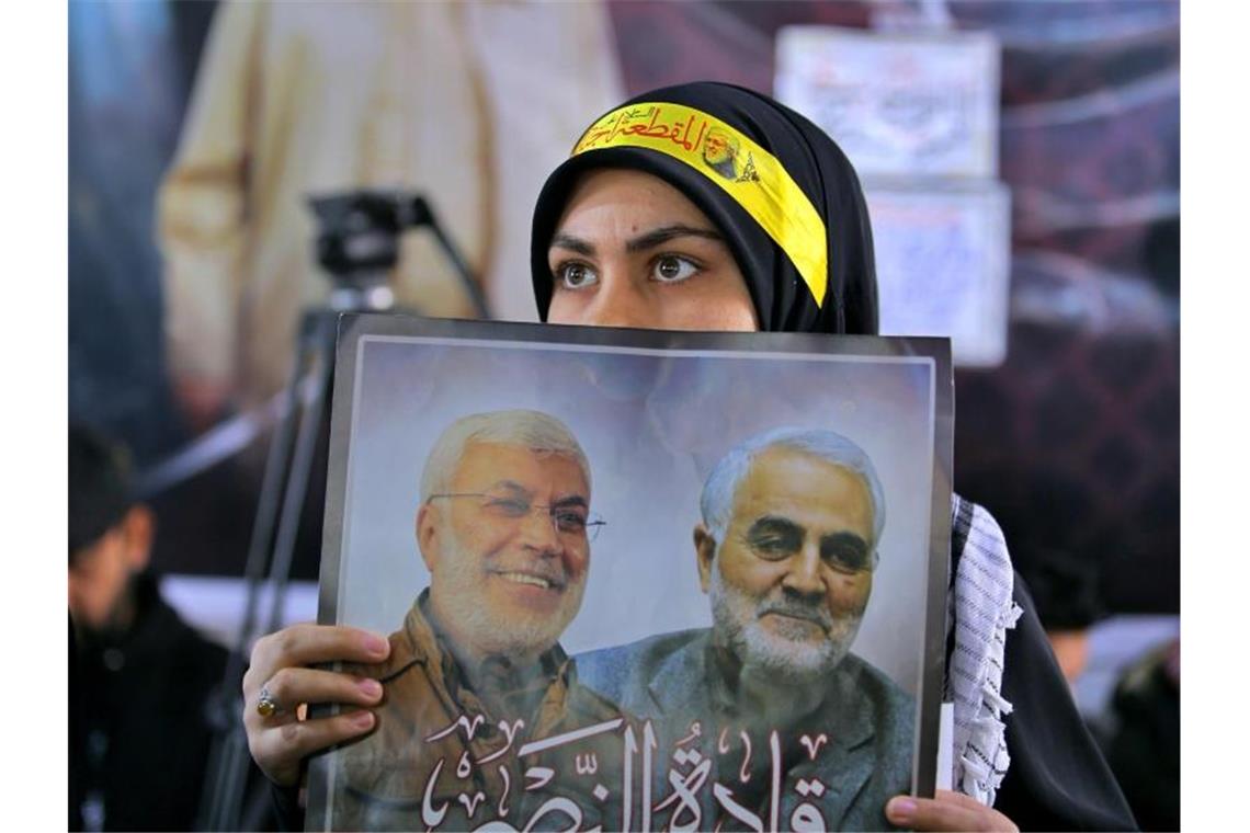Iran will über Interpol nach US-Präsident Trump fahnden Eine Frau hält ein Bild des einflussreichen irakischen Milizen-Anführers Abu Mahdi al-Muhandis (l) und des iranischen Top-Generals Ghassem Soleimani, die am 03.01.2020 durch die US-Armee bei einem Raketenangriff in der Nähe des Bagdader Flughafens getötet wurden, während einer Gedenkfeier. Foto: Anmar Khalil/AP/dpa