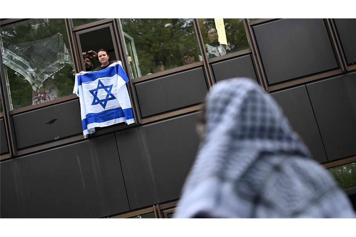Eine Frau hält eine Israelflagge aus dem Fenster: Die propalästinensische Demonstration auf dem Theaterhof der Freien Universität Berlin wird von Polizisten beobachtet.
