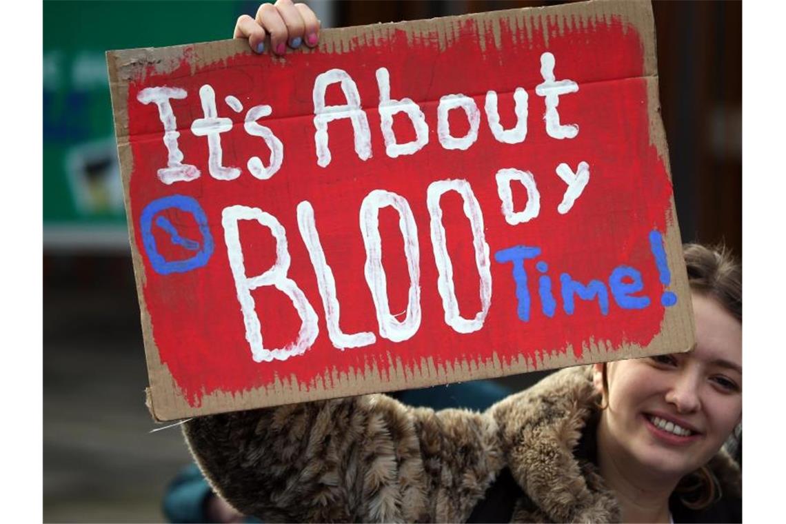Binden und Tampons in Schottland bald kostenlos erhältlich Eine Frau in Edinburgh hält bei einer Kundgebung ein Schild mit der Aufschrift "It's about bloody time!" (dt. Es ist verdammt noch mal an der Zeit) hoch. Foto: Andrew Milligan/PA Wire/dpa