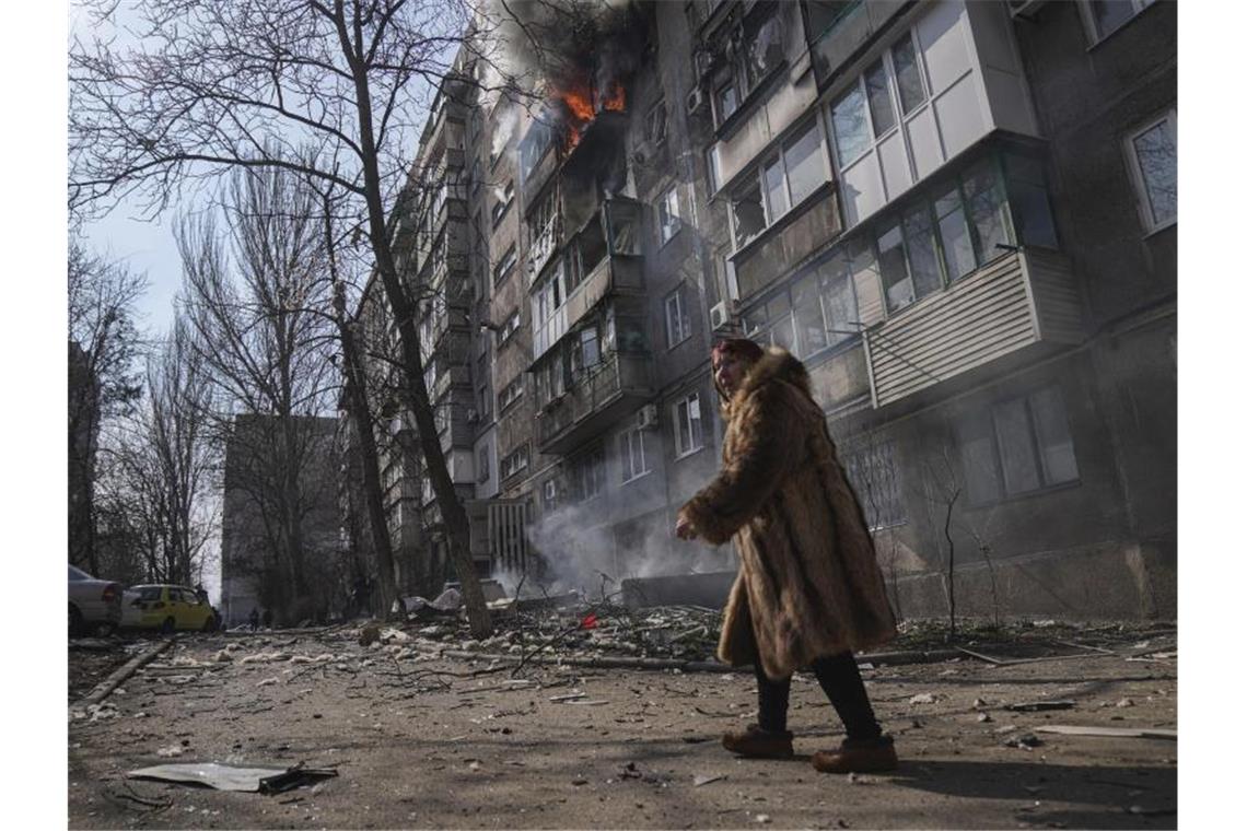 Kiew lehnt russisches Ultimatum für Mariupol ab Eine Frau in Mariupol geht an einem brennenden Wohnhaus vorbei. Foto: Evgeniy Maloletka/AP/dpa