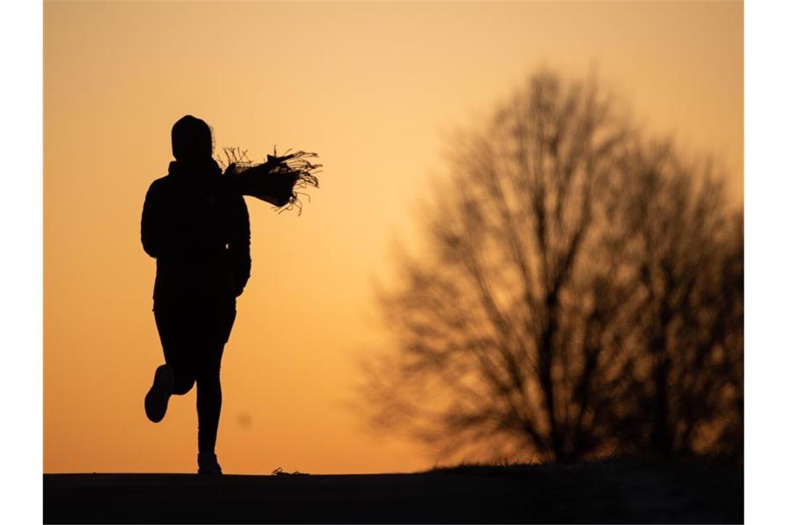Eine Frau joggt vor dem Sonnenaufgang. Foto: Sebastian Gollnow/dpa/Archivbild