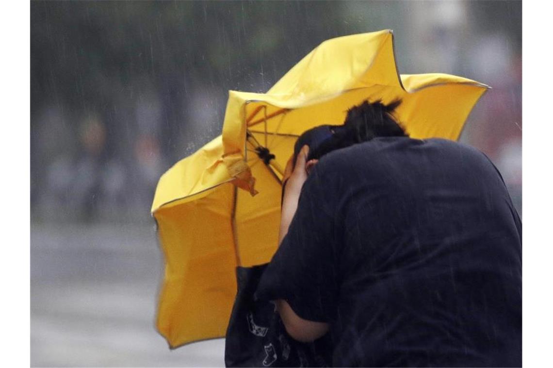Fastnachtsumzug in Baden-Baden abgesagt Eine Frau kämpft mir einem Regenschirm gegen Windböen. Foto: Chiang Ying-Ying/AP/dpa/Archivbild