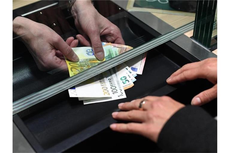 Eine Frau lässt sich in einer Bankfiliale am Schalter Bargeld auszahlen. Foto: Angelika Warmuth/dpa
