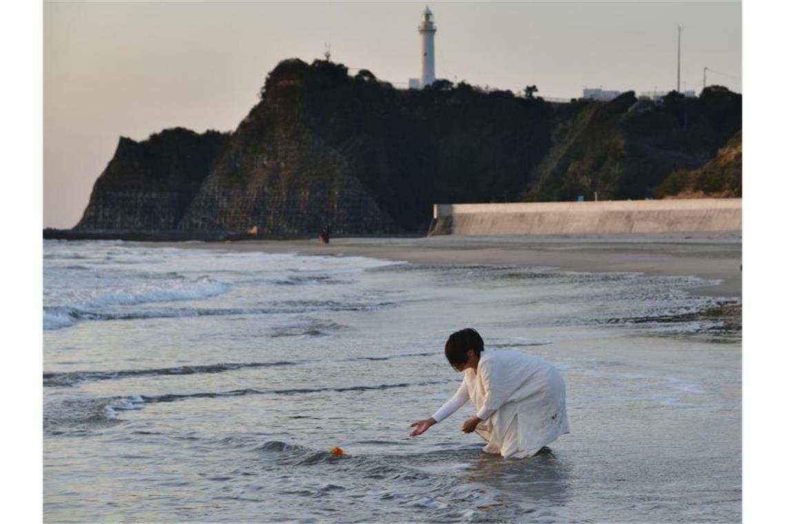 Eine Frau legt in Gedenken an die Opfer der Fukushima-Katastrophe Blumen an einem Strand in der nordostjapanischen Stadt Iwaki ab. Foto: ---/kyodo/dpa