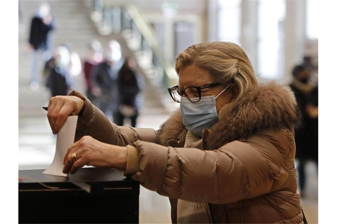 Eine Frau mit Mund-Nasen-Schutz gibt ihren Stimmzettel in einem Wahllokal in Lissabon ab. Foto: Armando Franca/AP/dpa