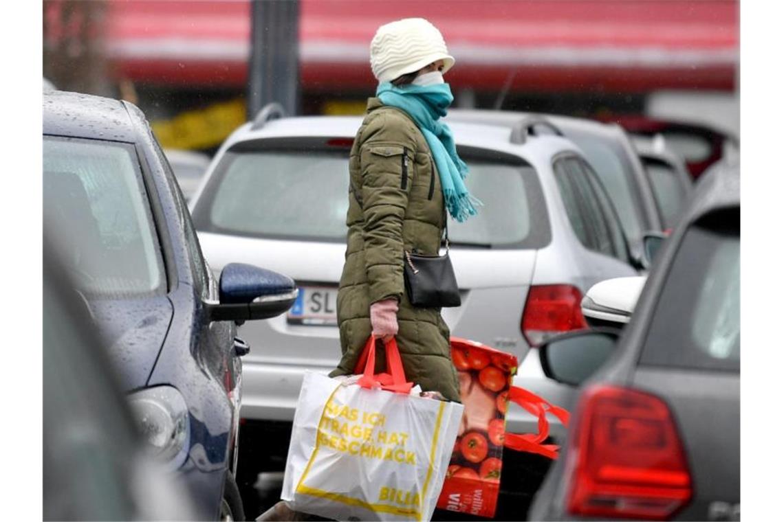 Eine Frau mit Mundschutz auf dem Parkplatz eines Einkaufszentrums in Salzburg. Foto: Barbara Gindl/APA/dpa