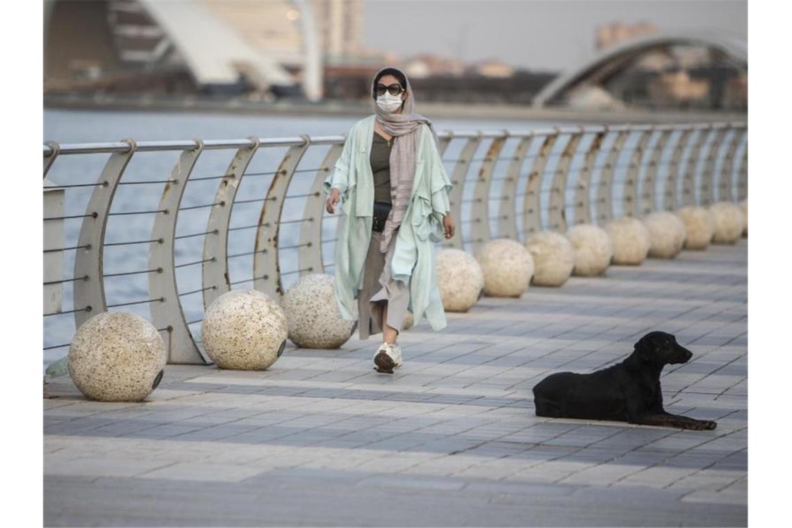 Eine Frau mit Mundschutz geht am Chitgar-See in Teheran spazieren. Die Zahl der Corona-Fälle im Iran steigt weiter an. Foto: Ahmad Halabisaz/XinHua/dpa